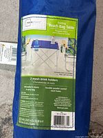 Product label showing brand "Mainstays" and product details including two mesh drink holders, foldable design, durable powder-coated steel frame, and carry bag.