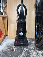 Full view of the upright black Bissell PowerForce vacuum cleaner on a floor with coiled power cord and hose attached.