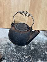 Side view of cast iron teapot kettle showing round body, spout, and coiled wire handle