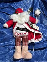 Full view of Santa Claus plush decoration standing on blue tarpaulin background.