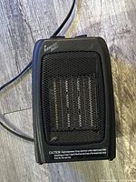 Front view showing metal mesh grill and heating components inside the compact black heater.