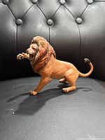 Side view of a lion figurine posed with one front paw raised, showing detailed mane and facial features.