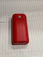 Red rectangular power bank shown on lined paper with a small square button on top surface.