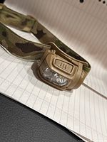 Front view of the tan-colored pro flashlight headlamp on a camouflage adjustable strap resting on a lined notebook.