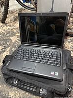Front view of black Dell laptop open, showing keyboard and screen with reflective surface. Laptop resting on a black carrying bag.