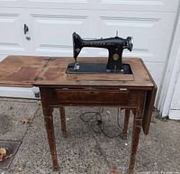 Full view of Singer sewing machine installed in wooden table; shows overall condition including table legs and surface wear