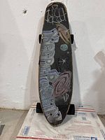 Full top view of skateboard showing space-themed grip tape with planets and stars drawn on it.
