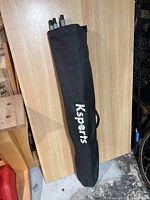 Black fabric carry bag with black handle and white Ksports logo on side, standing upright on wooden surface.