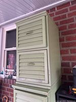 Front view of light green wooden cabinet with two slatted doors, showing handles and wear.