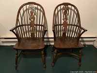Front view of two solid wood barrel back chairs featuring high backs with multiple spindles, curved armrests, and turned legs.