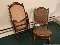 Two folding solid wood rocking chairs: one standing upright with burgundy upholstery, one folded with cream upholstery fabric.