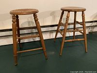Two oak counter height stools side by side showing the difference in seat style: one with a caned seat and the other with a solid wood seat. Both have turned legs and stretcher supports.