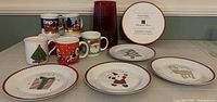 Photo with five Christmas-themed coffee mugs, four lunch plates showing different Christmas designs, and one tall red glass vase.