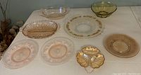Assorted coloured glass serving plates and bowls displayed on a table showing various shapes and colours including amber, clear, green, and pink glassware.