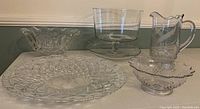 Overview of all glass serving pieces including platter, footed bowl, pitcher, and two fluted bowls