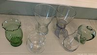 Overview of the six glass vases including clear and green varieties, showing various shapes and sizes on a light surface.