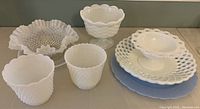 Photo showing the full set of 3 glass plates (white opaque, blue opaque, white rimmed), 1 wavy hobnail bowl, 2 footed bowls, and 2 small hobnail plant pots on a surface.