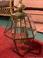 Photo of entire brass and glass light fixture showing polygonal glass panels and brass framing.
