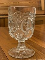Clear antique pressed glass water goblet standing on wood surface, showcasing overall shape and detailed textured patterns on bowl and base.