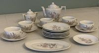 Full view of the child-sized china teaset including teapot, sugar bowl, six plates, five teacups with matching saucers, and oval serving platter on a neutral surface