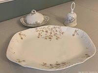 Photo showing top view of china platter, covered soap dish, and decorative bell with rose pattern placed on table.
