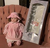 Full view of doll seated next to original box on pink chair showing the doll and box condition