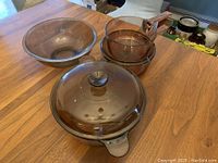 Overall set of purple glass cookware including the Dutch oven, three pots, and one large bowl shown on wooden table