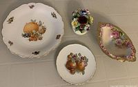 Lot showing two decorative plates with fruit and floral motifs, a footed bowl with floral design and gold trim, and a small china flower bouquet figurine