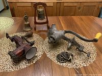 Two vintage metal food grinders displayed on a table, showing red grinder with attachments and silver grinder with extra plates.