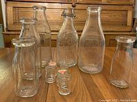 Photo showing all five glass creamers and five milk bottles, various vintage styles including two with lids.