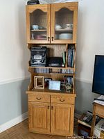 Tall oak cabinet in natural finish with glass front upper cabinet doors, middle open shelves, two drawers and lower cabinets. Items on/in cabinet not included.