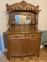 Front view of the solid oak hutch showing the mirror, carved trim panel, 2 drawers, 2 doors, and side shelves with decorative items on top (not included).