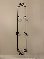 Front view of black metal wall plate rack showing four pairs of scrolled hooks for holding plates.