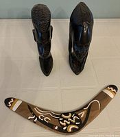 Top-down view showing two carved dark wood tribal statues standing upright and a decorated wooden boomerang placed in front of them.