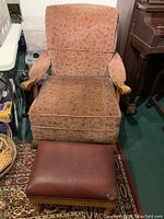 Front view of vintage floral upholstered chair with wooden armrests and red leather ottoman.