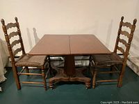 Full front view of the antique solid wood games table with 4 matching ladder back rush seat chairs arranged around it.