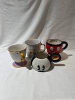 Four Disney-themed mugs shown together on a white backdrop