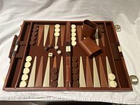 Open backgammon board showing full layout with checkers, dice cups, dice, and doubling cube arranged inside playing surface.