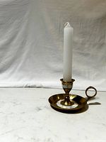 Single brass candlestick holder with mother of pearl inlay and white taper candle upright against neutral background.