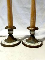 Photo showing two brass taper candlestick holders with mother of pearl accents. Each holder has scalloped edges, a round mother of pearl base, and tall brown taper candles.