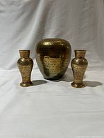 Full set of one large solid brass vase and two smaller floral patterned brass bud vases standing on white background.