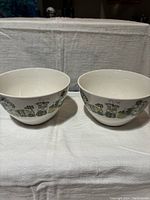 Two white ceramic bowls side by side on a white pressed cloth with botanical pattern around the exterior.