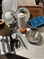 Photo showing a collection of various kitchen utensils, ceramic items, silicone ice cube trays, cutting board, and mixing bowls