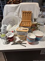 Full overview of various kitchenware items arranged on a countertop, including bowls, storage jars, butter dish, cheese set, mugs, and utensils.