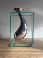 Front view of the modernist aluminum and glass vase showing the sleek teardrop shape inside the clear glass box frame.