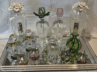 Wide shot showing entire collection of 13 perfume bottles on mirrored tray with velvet backing including green and gold Murano bottle, crystal bottles, and two porcelain rose stopper bottles.