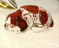Side view of porcelain puppy paperweight showing brown and white fur with gold accents, lying curled up sleeping.