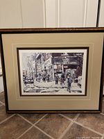 Framed winter street scene art print showing people and storefront with 'Greeting Cards' sign on snowy Queen Street West, Toronto.
