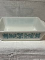 Full view of the white opaque square casserole dish with turquoise Amish Butterprint design on side.