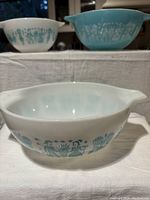 Photo showing a white Pyrex Cinderella bowl with teal Amish Butterprint design in front, turquoise bowl with white design in back, and another white bowl with teal design placed together.